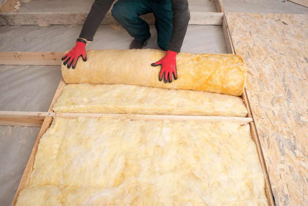 A man wearing red gloves carefully rolling insulation on the floor, preparing the space for enhanced thermal protection and energy efficiency.
